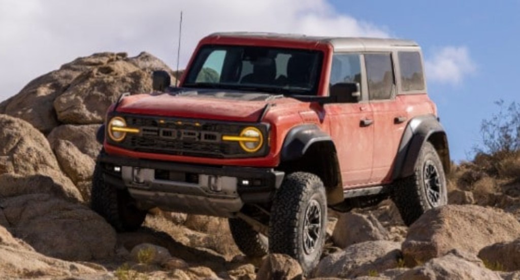 A red 2022 Ford Bronco Raptor off-road SUV is driving over rocks. 
