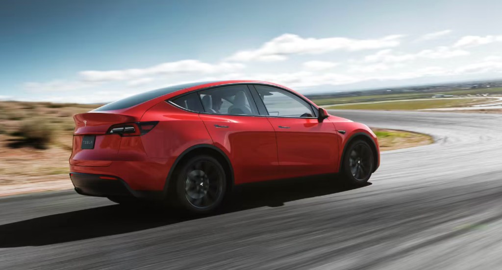 A red Tesla Model Y is driving down the road. 