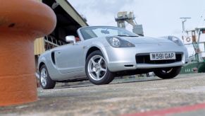 A silver Toyota MR2 in an outdoor environment with buildings around.