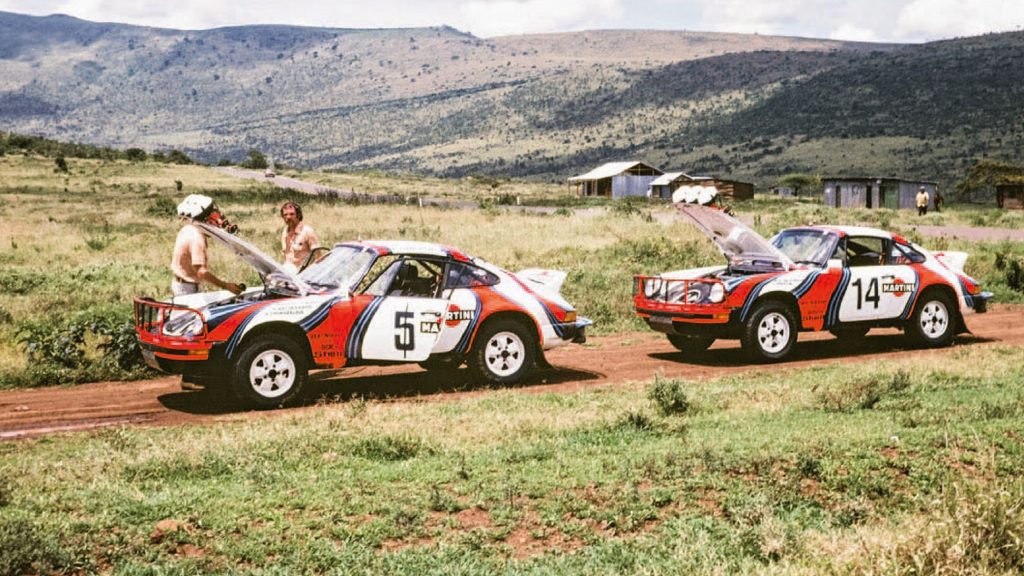 Two Porsche 911 SC 3.0s at the 1978 East African Safari Rally on a dirt road by a field and mountains