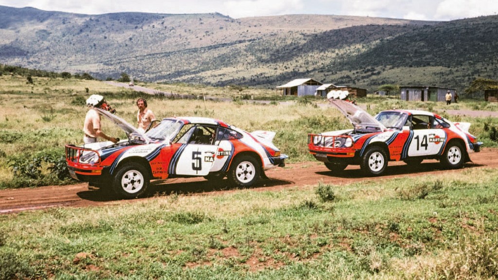 Two Porsche 911 SC 3.0s at the 1978 East African Safari Rally on a dirt road by a field and mountains