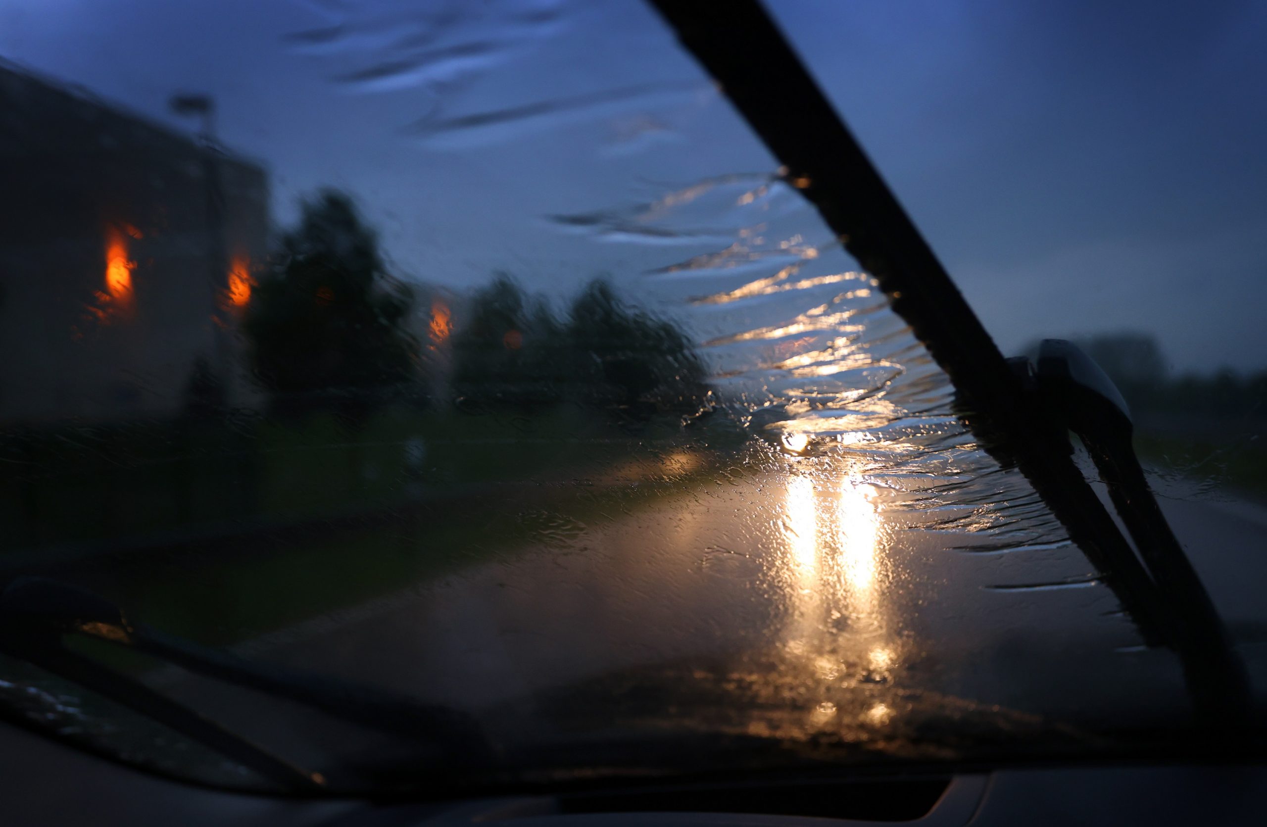 Windshield wipers cross a windscreen on a rainy night