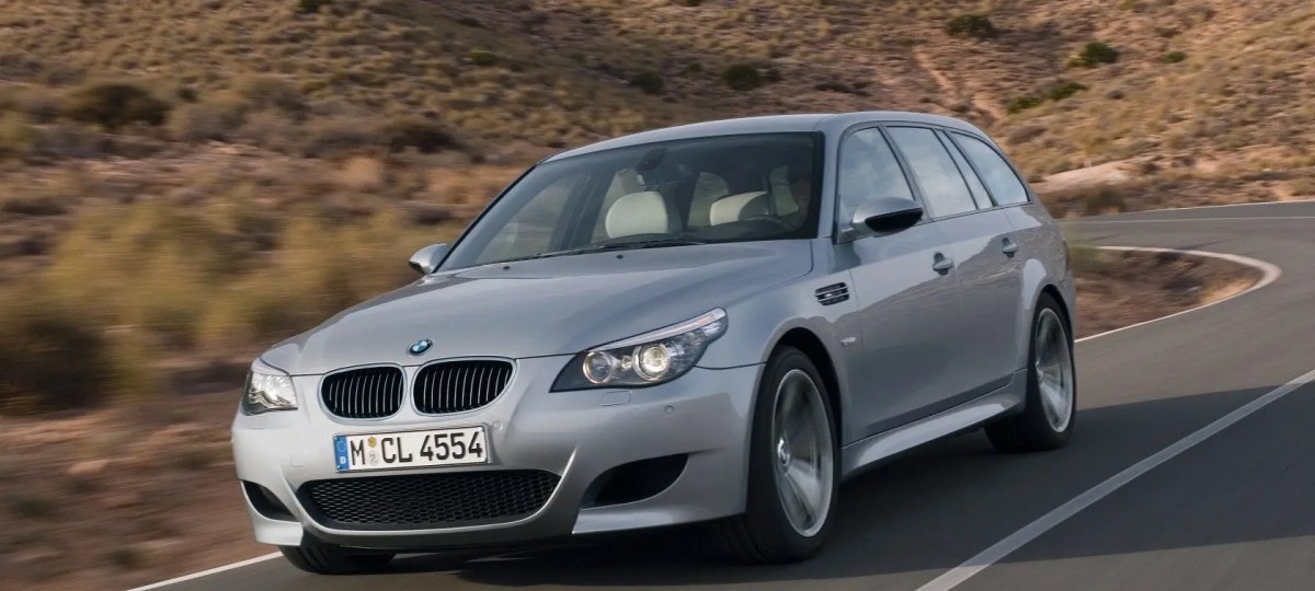 A 3/4 front view of a silver BMW E61 M5 Touring driving on a curvy road.