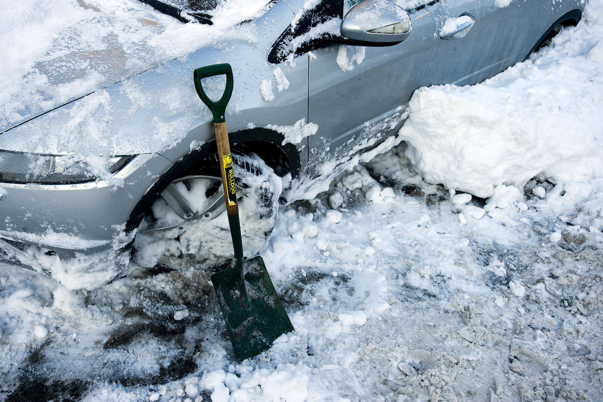 A car covered in ice and snow sits next to a shovel