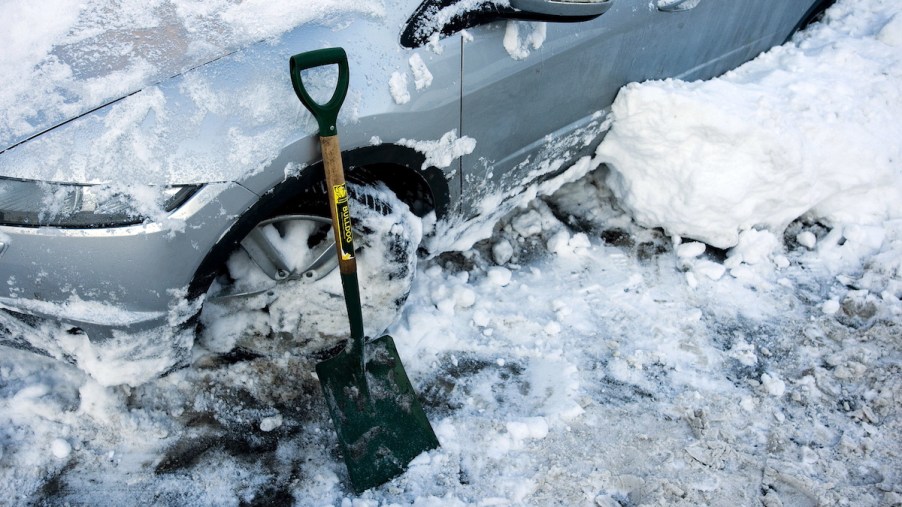 A car covered in ice and snow sits next to a shovel