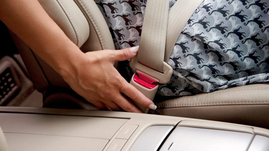 A lady unbuckles her seat belt in a car
