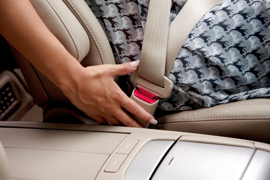 A lady unbuckles her seat belt in a car