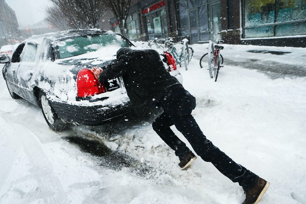 A man pushes his car out of deep snow.