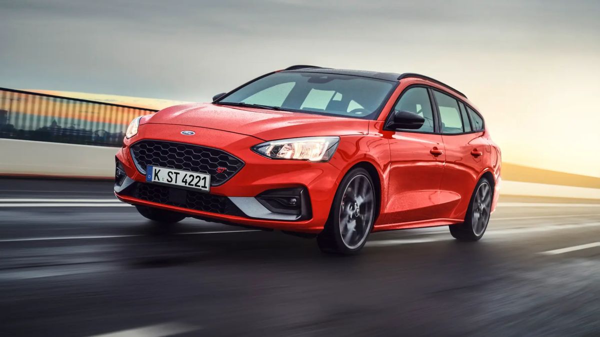 A 3/4 front view of a red 2020 Ford Focus ST Estate driving on a wet road with a guard rail behind it.