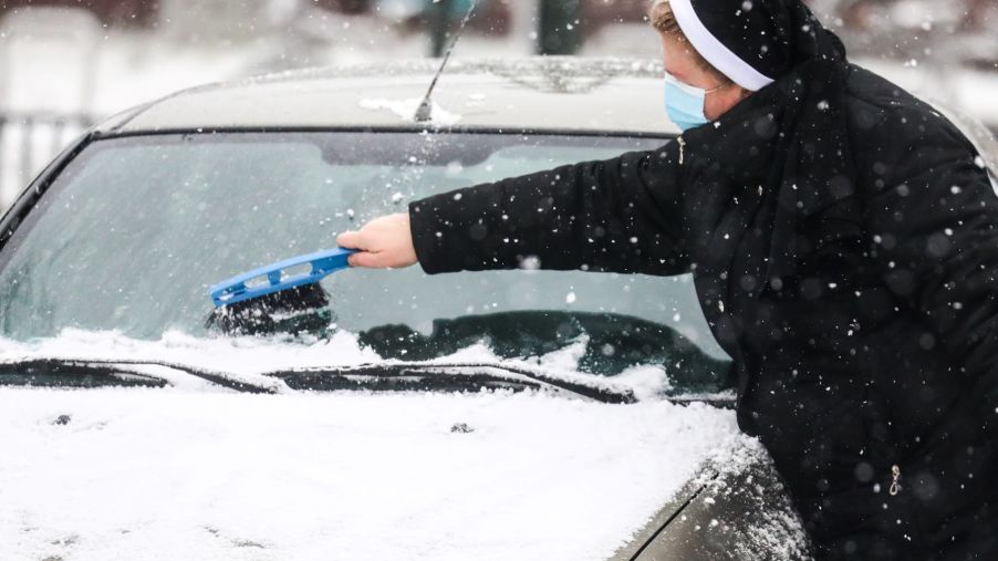 A nun clearing snow off a car windshield during winter in Krakow, Poland