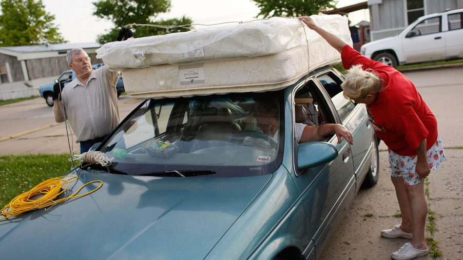 an older couple straps a mattress to a car roof