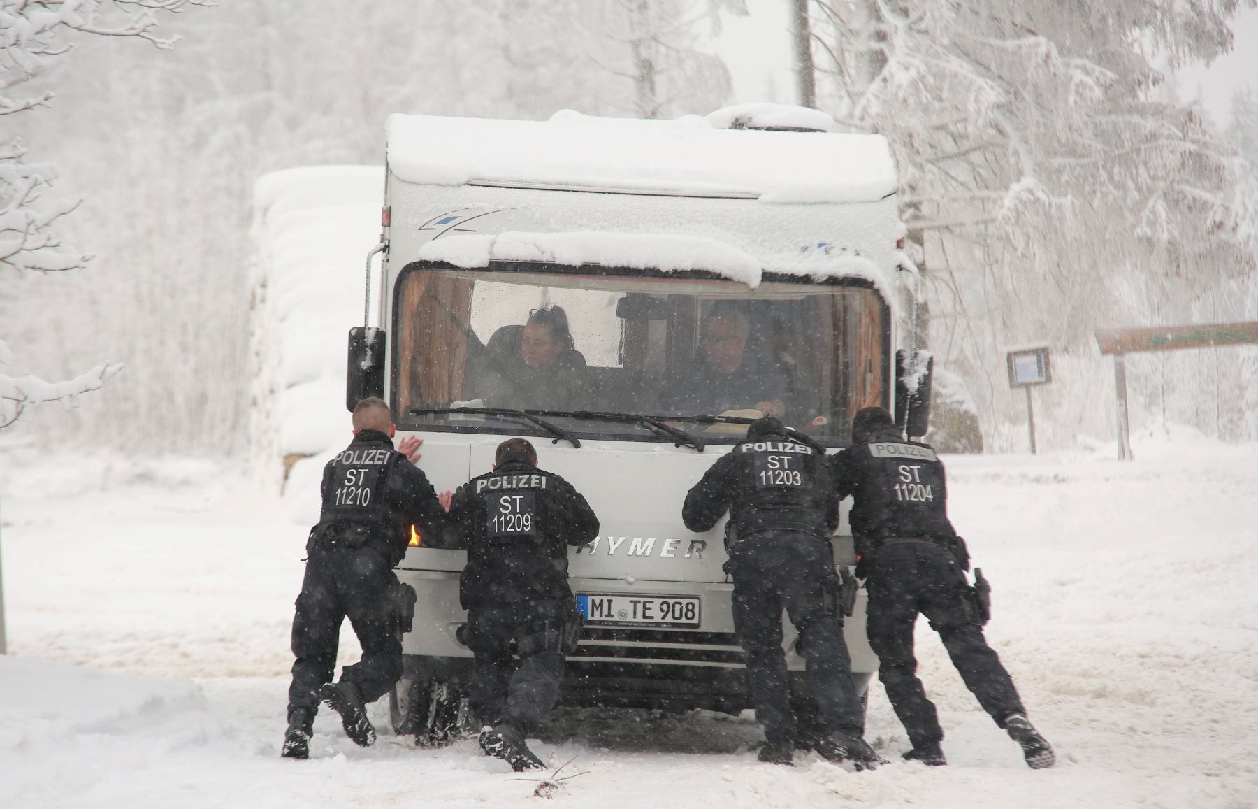 A camper RV motorhome stuck in winter snow and being pushed by police officers in the Harz Mountains