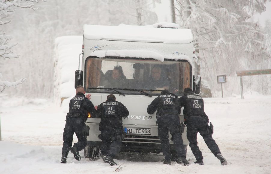 A camper RV motorhome stuck in winter snow and being pushed by police officers in the Harz Mountains