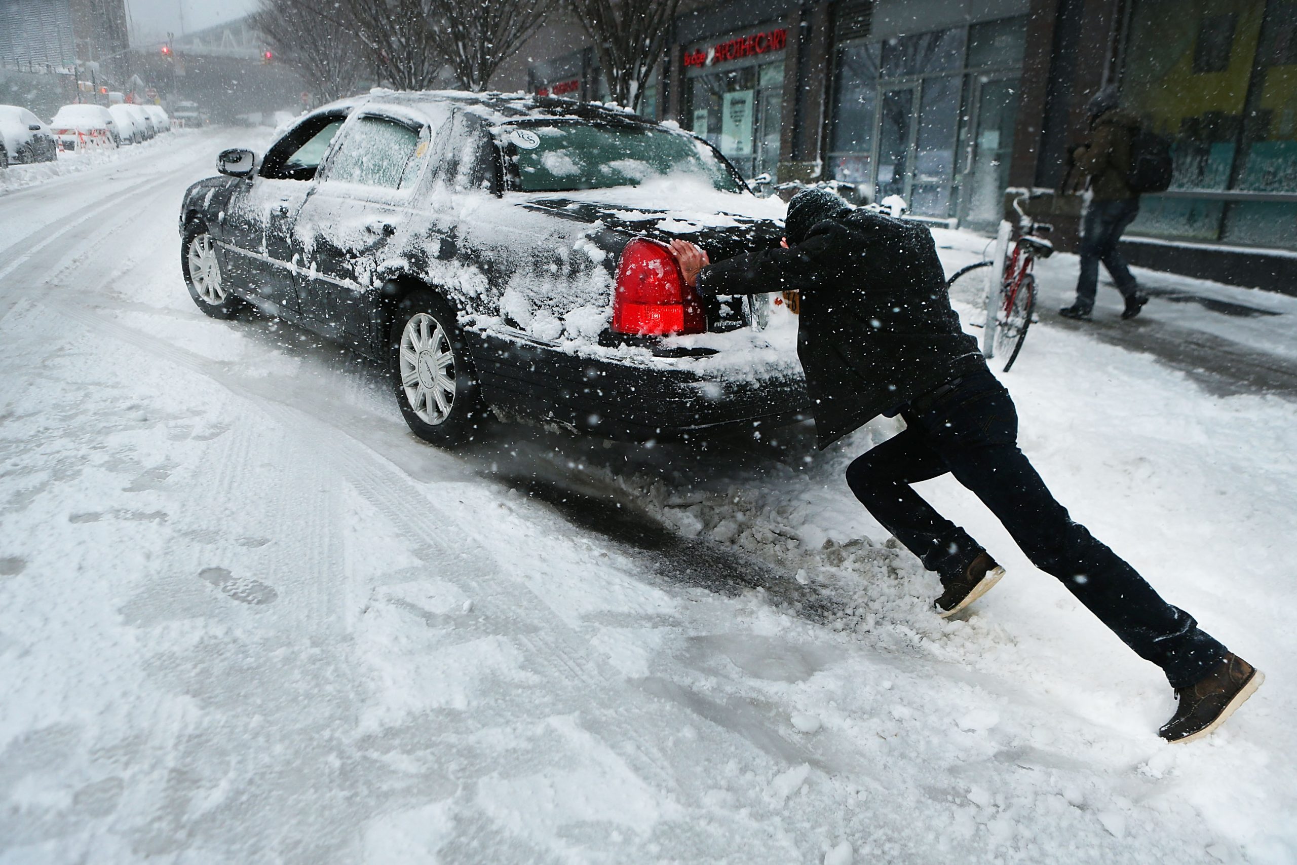 A man pushes a car stuck in the snow during a blizzard