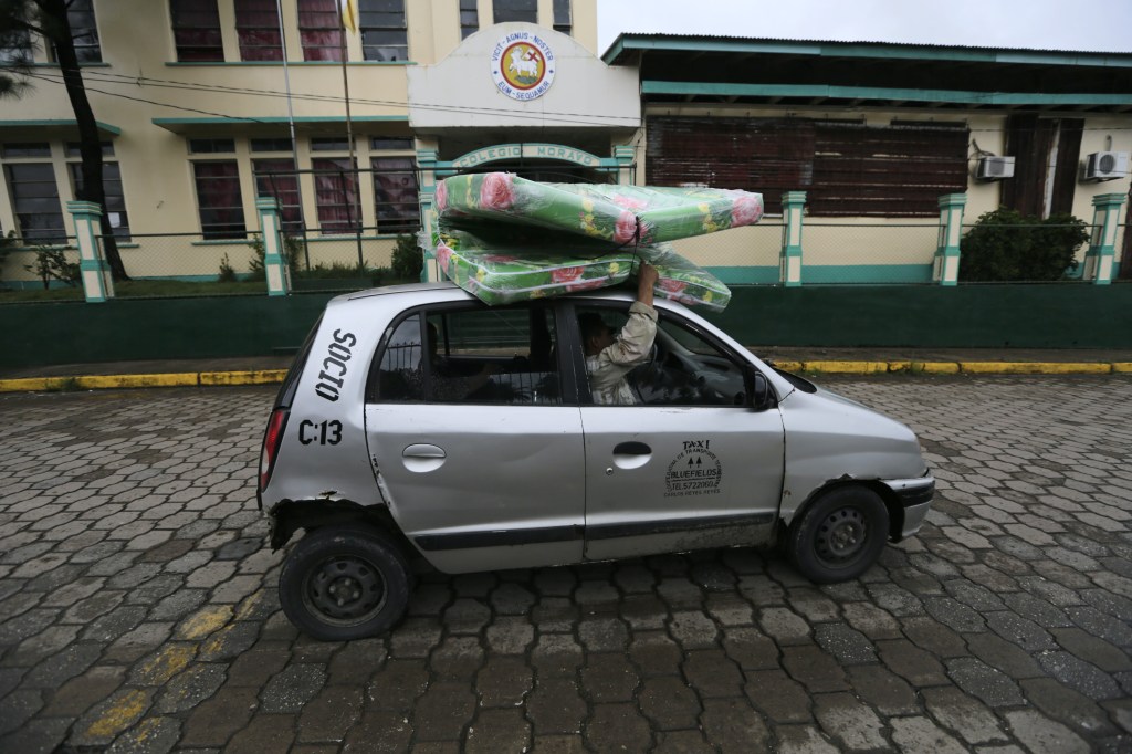 A man carries a mattress on the roof of a taxi. 