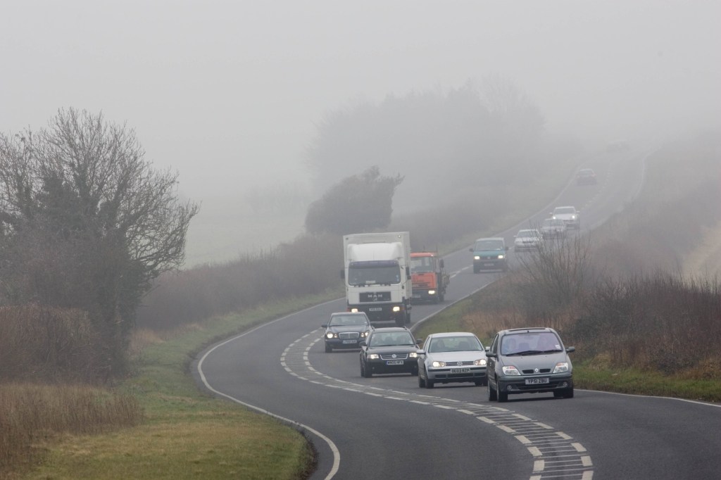  Cars and lorries drive along a foggy road.