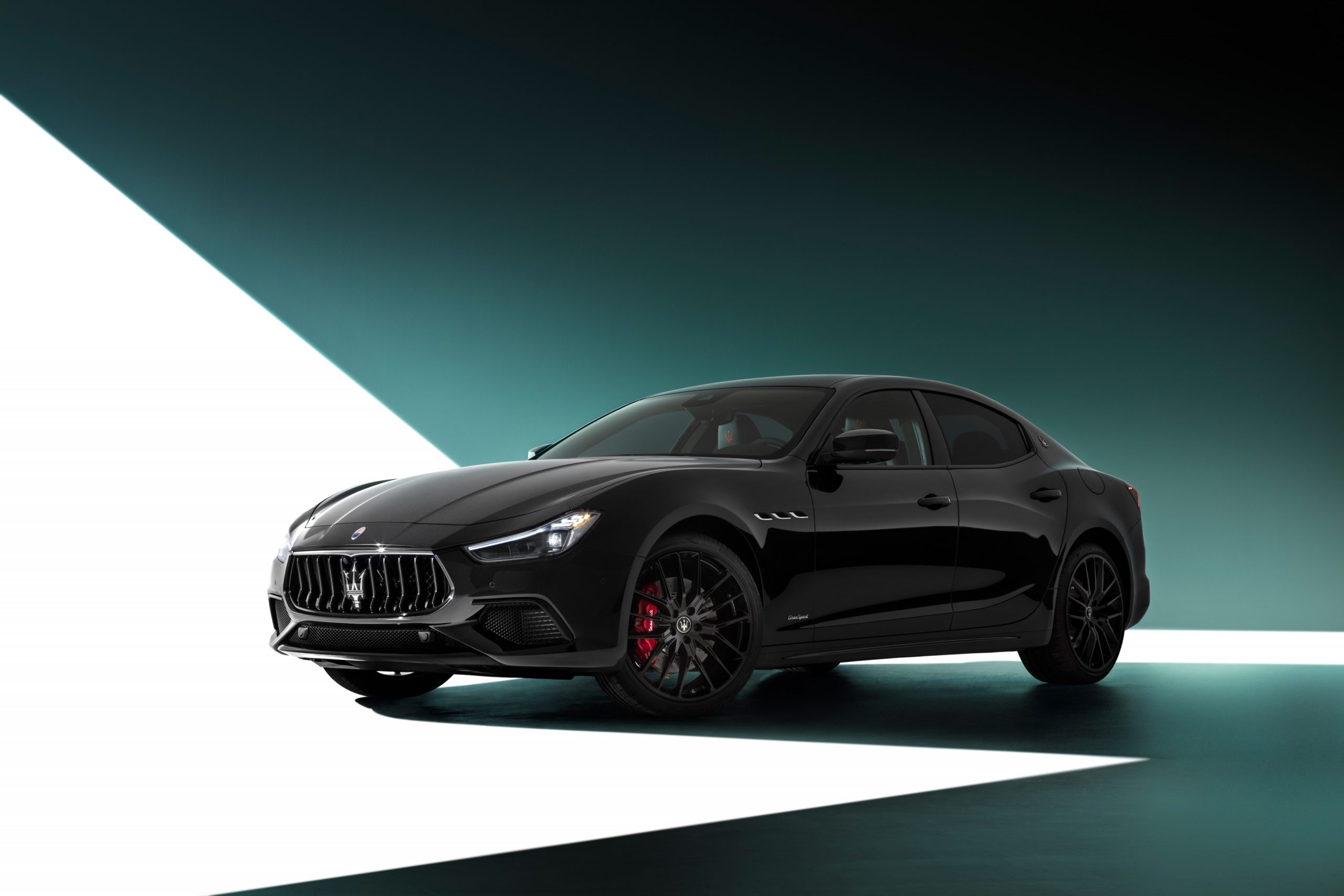 A 3/4 front view of a black Maserati Ghibli sedan with a white and green studio background