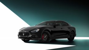 A 3/4 front view of a black Maserati Ghibli sedan with a white and green studio background