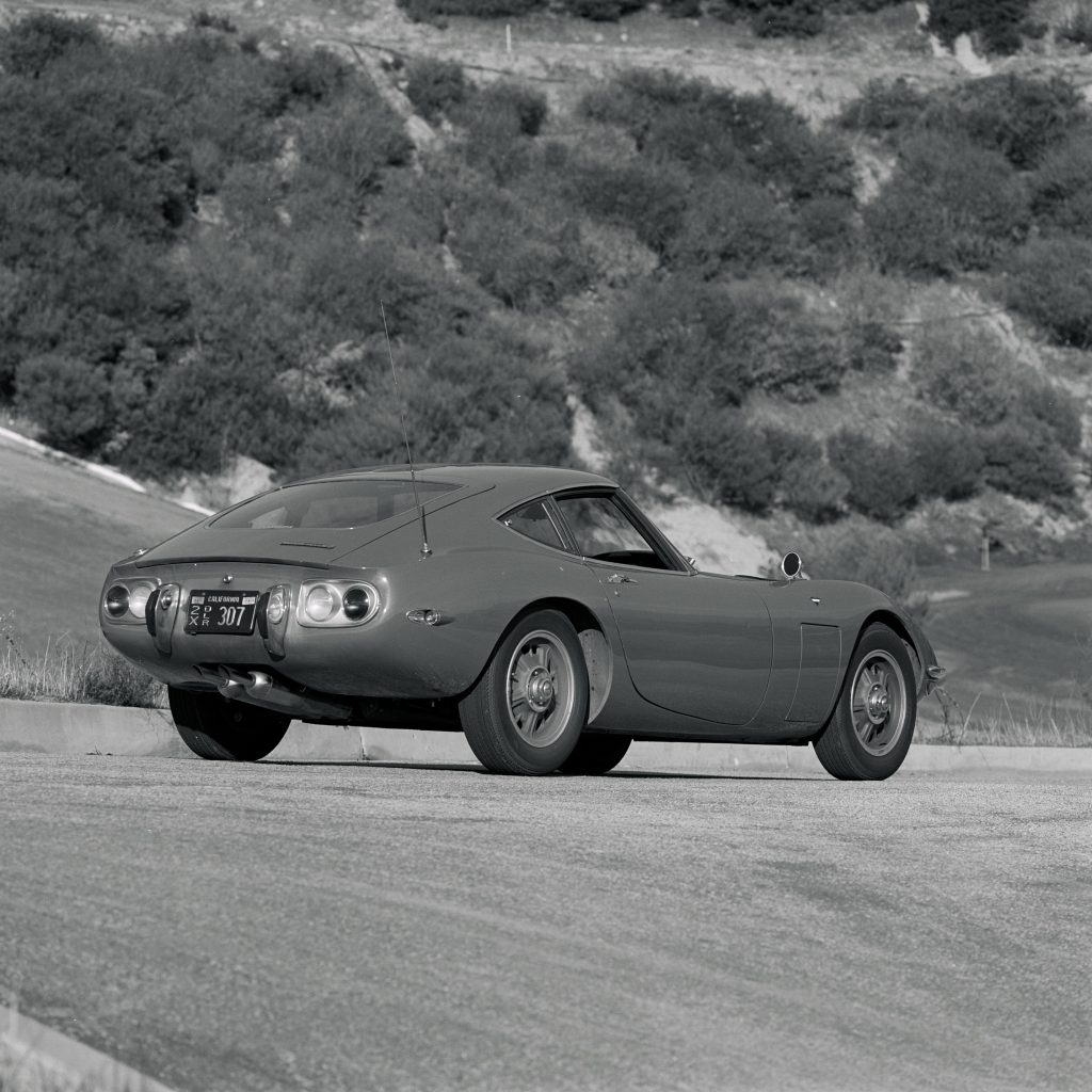 A rear 3/4 view of a 1968 Toyota 2000GT on a curving road