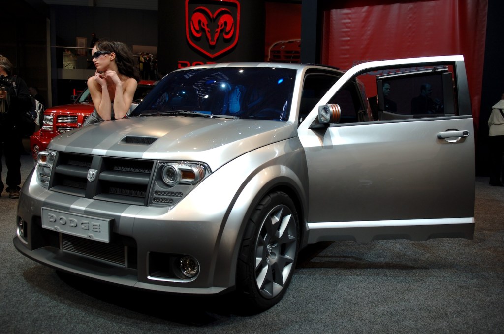 Prototype of a Dodge Hornet crossover car prototype parked on the stage at an auto show with a model leaning on the hood.