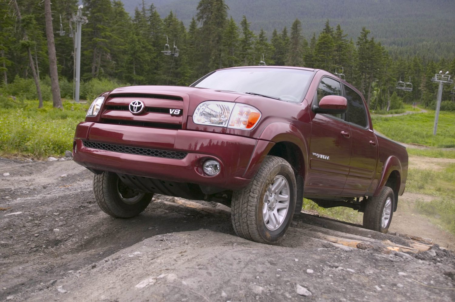 Red 2006 Toyota Tundra climbing a mountain trail in front of a ski lift and wooded hills.