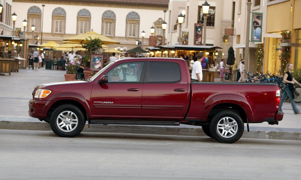 Red, four door pickup truck parked in a business district of a town, in front of a cafe, as people walk by on the street.