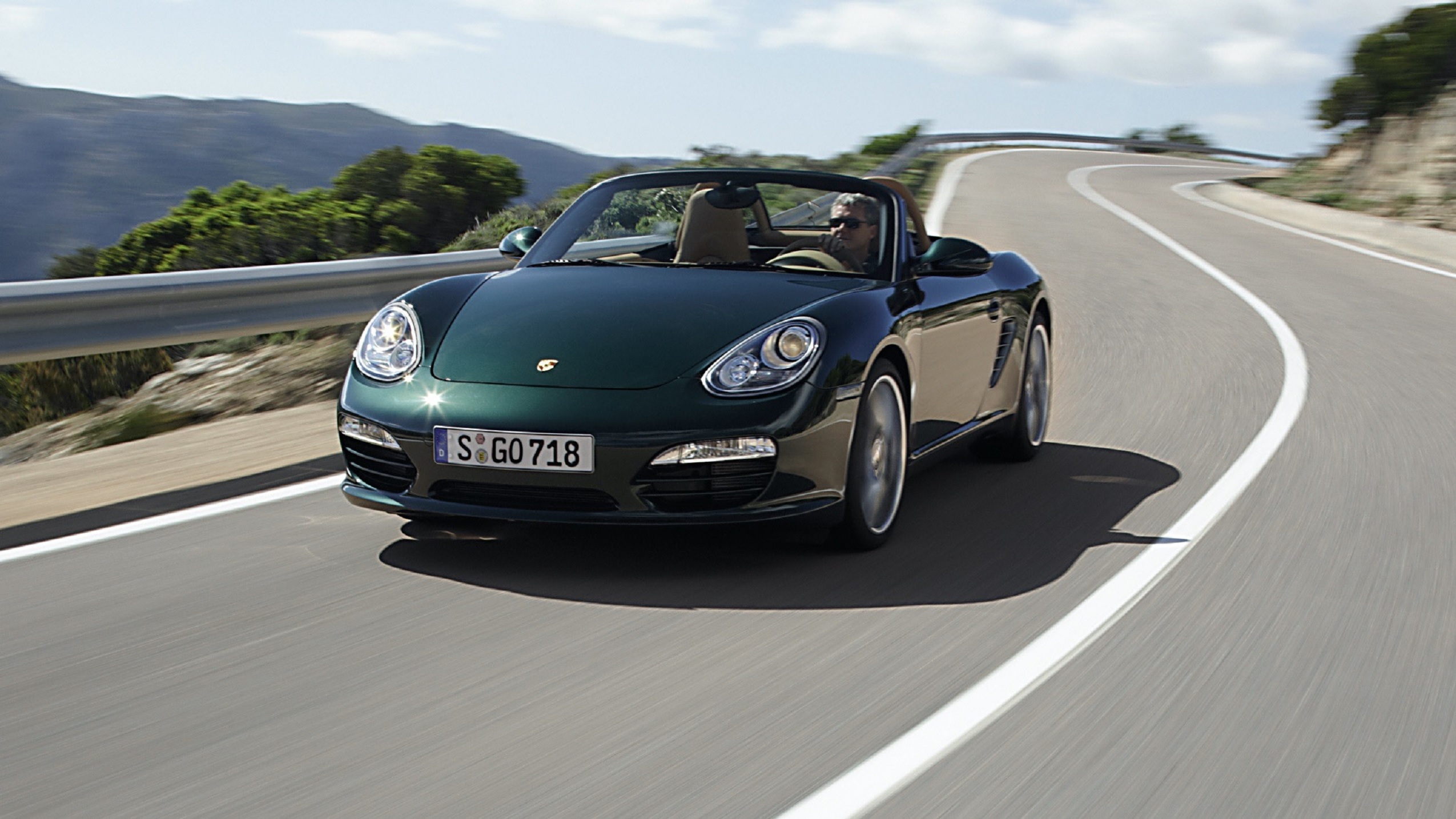 A green 2008 987 Porsche Boxster driving down a canyon road