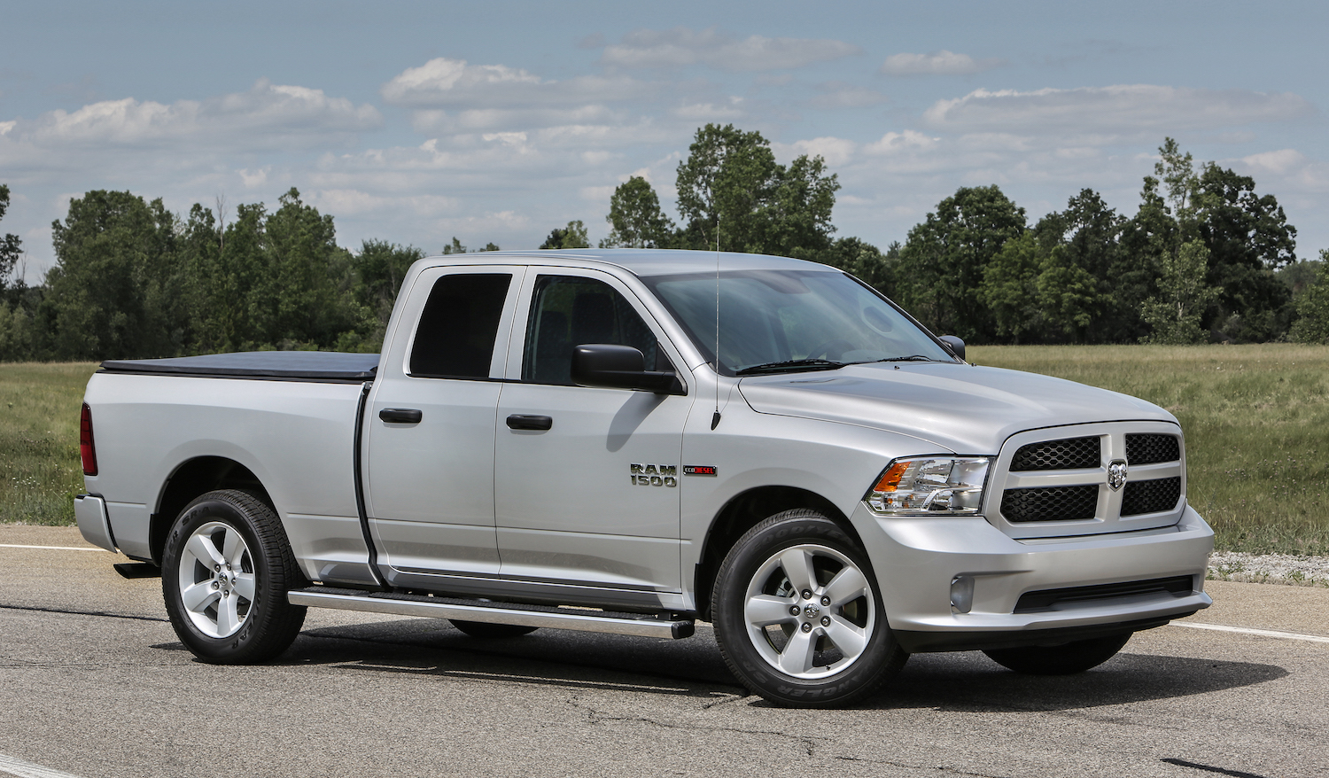Promo photo of a silver 2018 Ram truck parked on a street in front of a row of trees.
