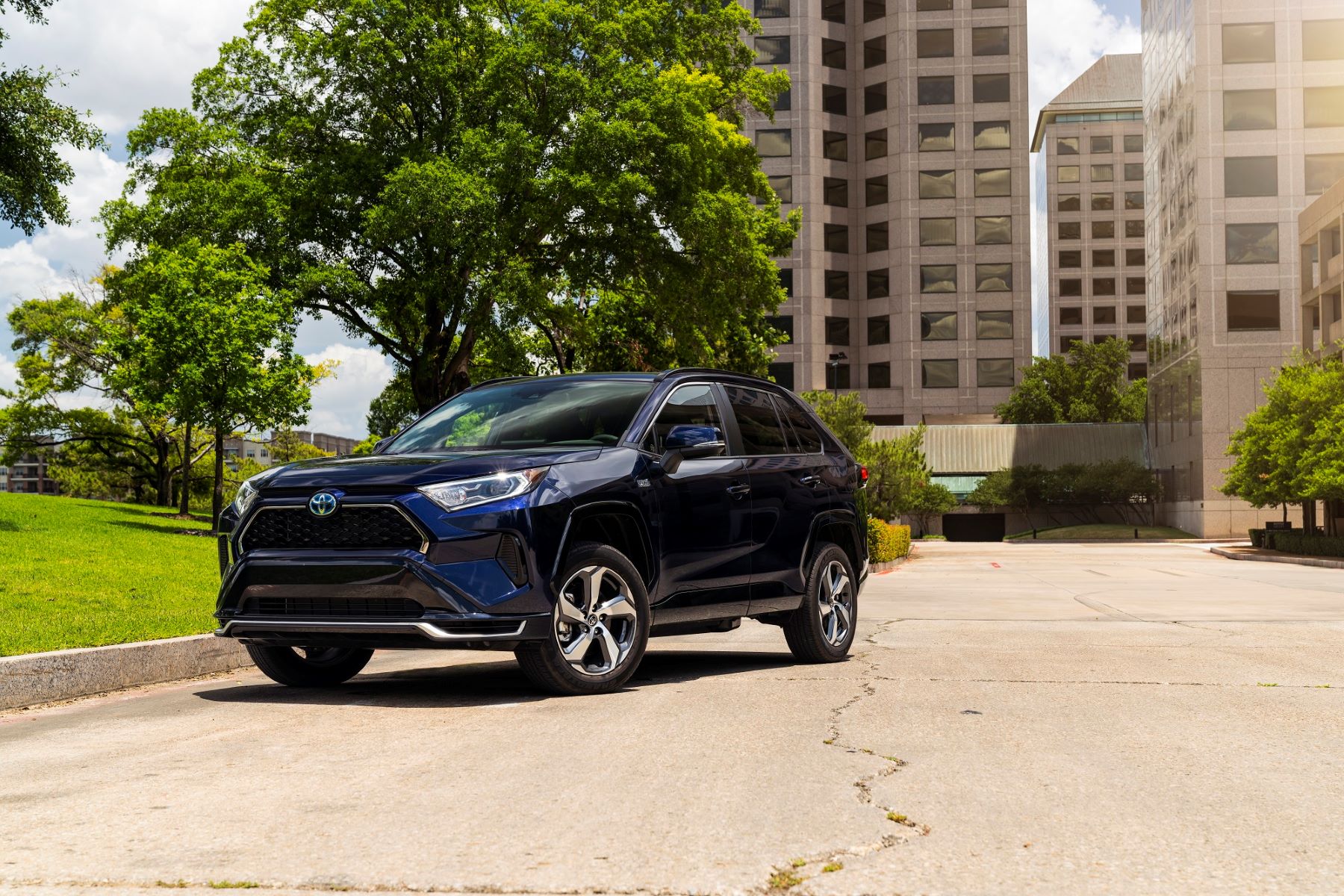 The 2021 Toyota RAV4 Prime plug-in hybrid (PHEV) compact SUV model parked near a grass field outside of windowed skyscrapers