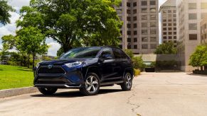 The 2021 Toyota RAV4 Prime plug-in hybrid (PHEV) compact SUV model parked near a grass field outside of windowed skyscrapers