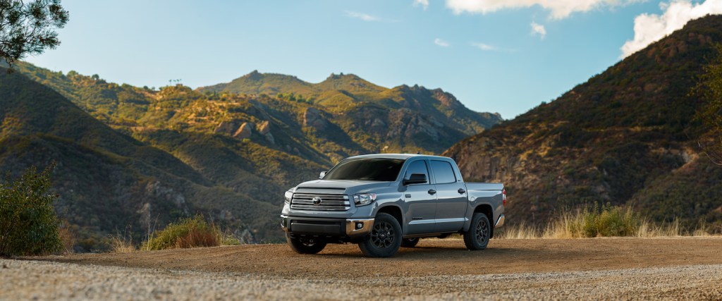 Promo shot of a gray Toyota Tundra pickup truck parked on dirt with mountains in the background.