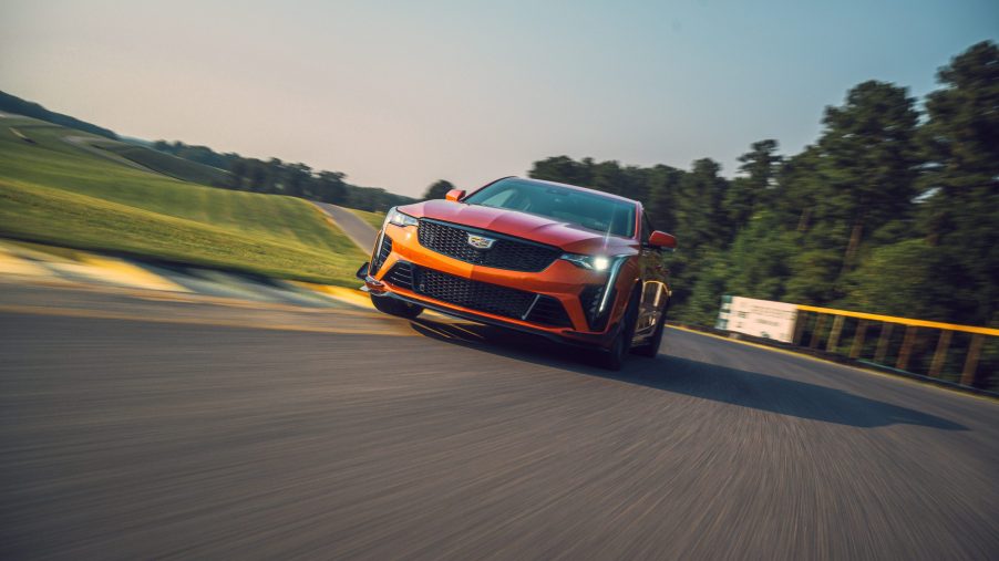 A front view of an orange 2022 Cadillac CT4-V Blackwing cornering on a race track with trees in the background