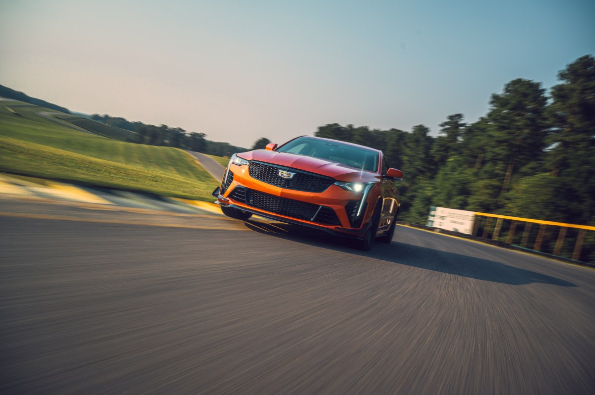 A front view of an orange Cadillac CT4-V Blackwing cornering on a race track with trees in the background