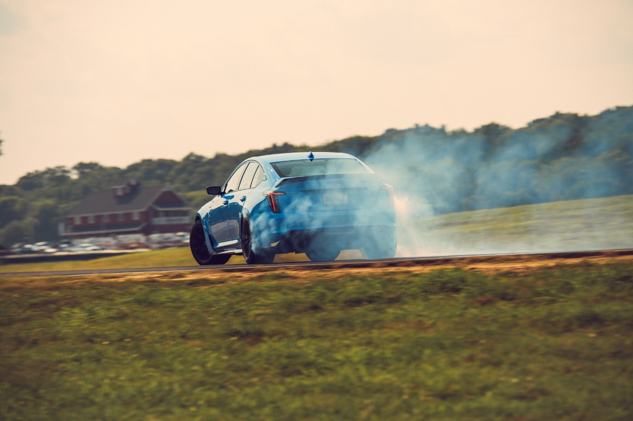 Electric Blue Cadillac CT5-V Blackwing drifting around a corner on a race track shot from behind