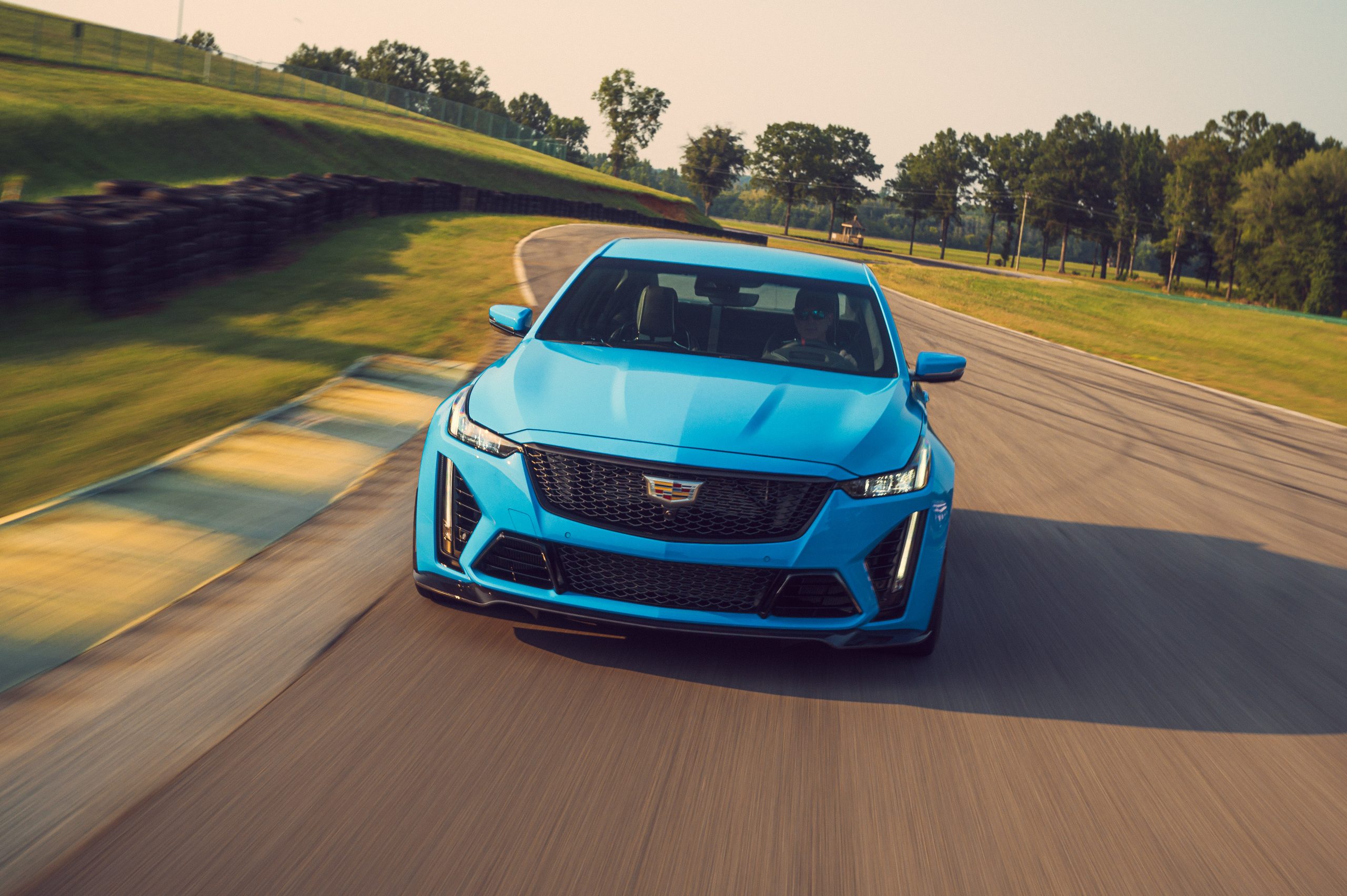 A front view of a blue 2022 Cadillac CT5-V Blackwing cornering on a race track with trees in the background.