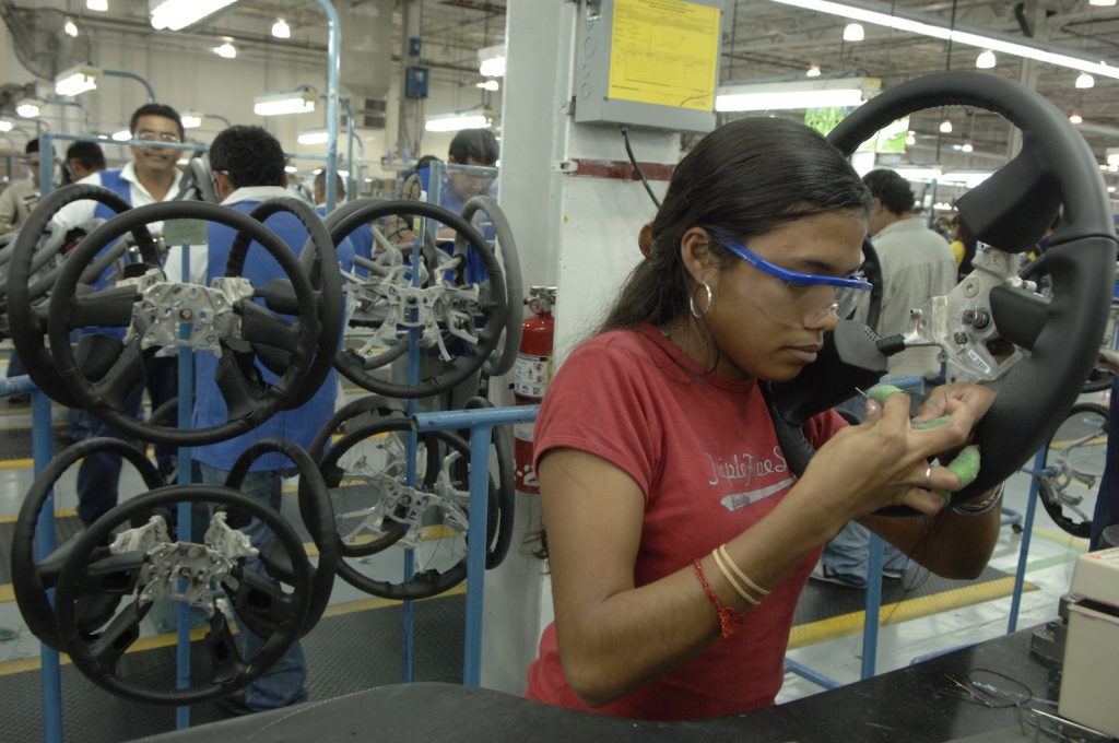 A Mexican woman on an assembly line with a needle and thread upholstering a GMC Sierra steering wheel.