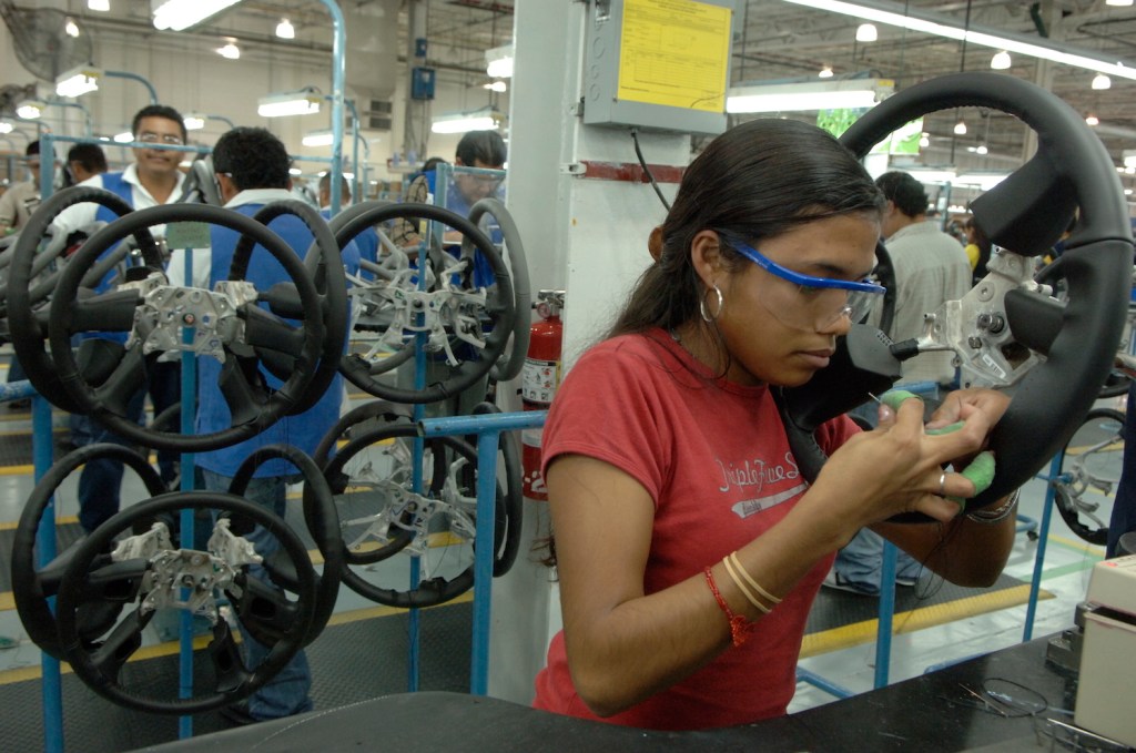 A Mexican woman on an assembly line with a needle and thread upholstering a GMC Sierra steering wheel.