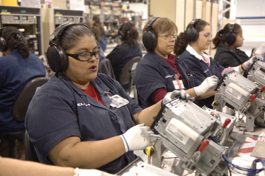 A row of women at an assembly line building car stereos.