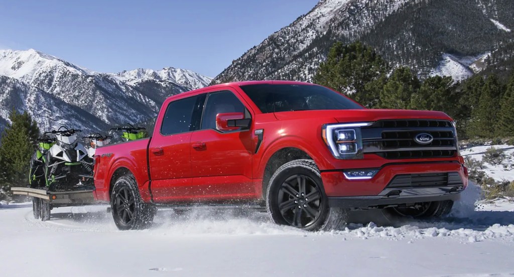 A red 2022 Ford F-150 is towing snowmobiles in the snow. 