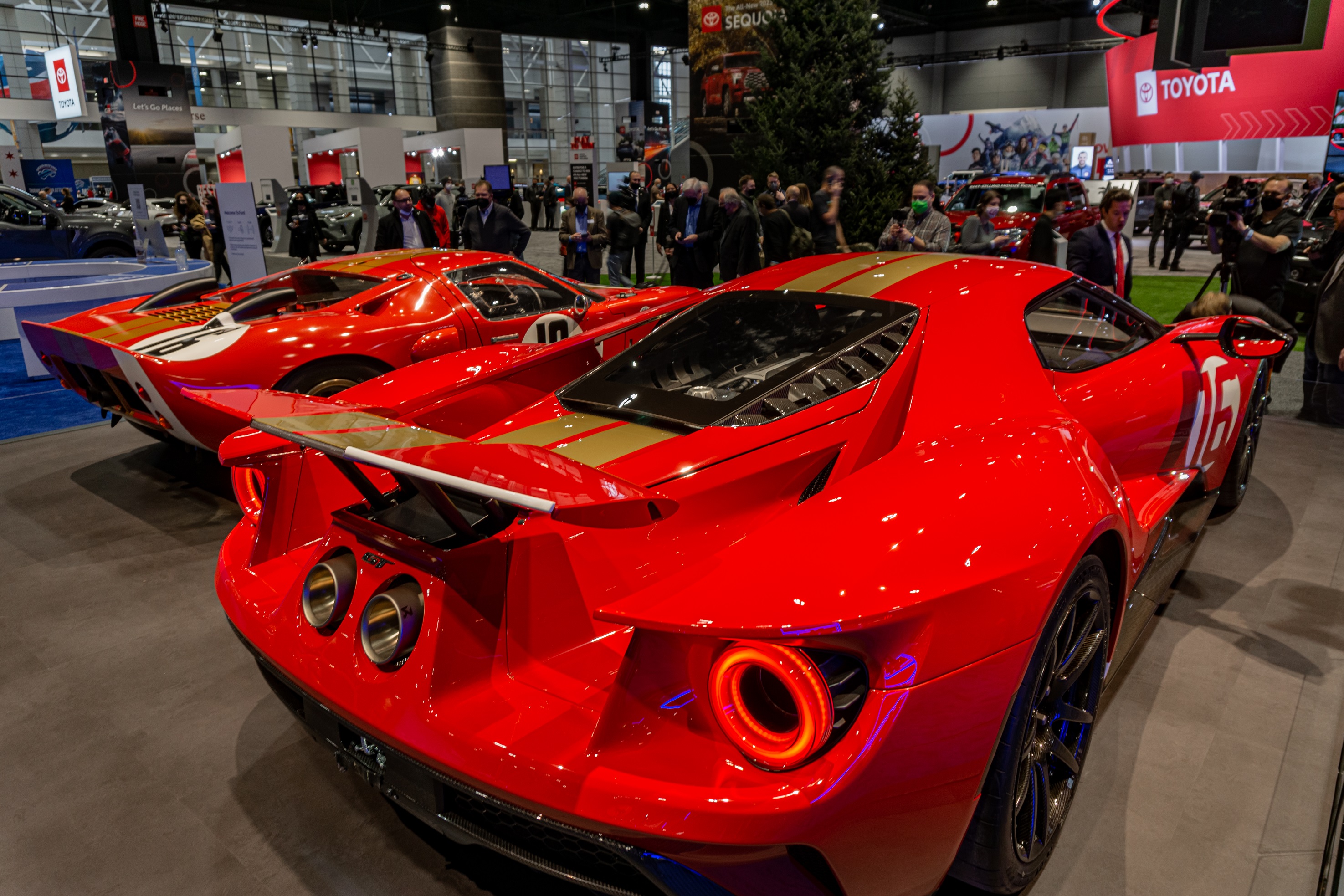 The rear 3/4 view of the red-and-gold 2022 Ford GT Alan Mann Heritage Edition next to the red-and-gold 1966 Ford GT40 Mk I Lightweight 'AM GT-1'