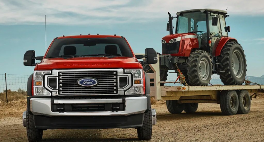 A red Ford Super Duty heavy duty pickup truck is towing a small tractor. 
