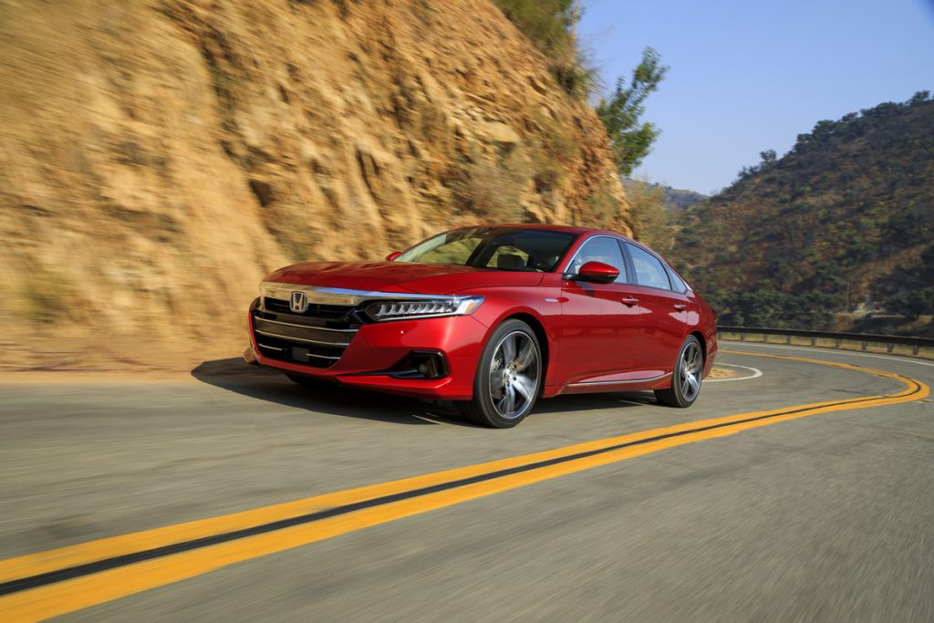 A red 2022 Honda Accord Hybrid traveling on a two-lane mountain highway