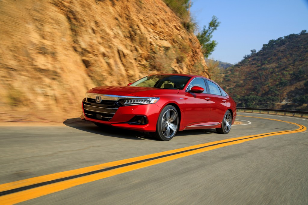A red 2022 Honda Accord Hybrid traveling on a two-lane mountain highway