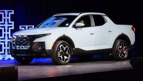 A white 2022 Hyundai Santa Cruz in front of a black background with a lite blue pattern.