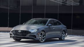 The 2022 Hyundai Sonata compact sedan model with a gray paint color parked in front of a black glass wall