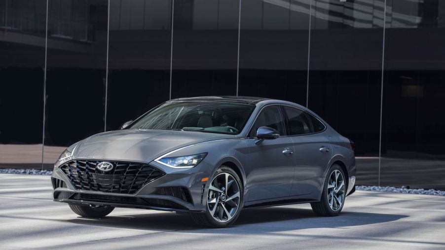 The 2022 Hyundai Sonata compact sedan model with a gray paint color parked in front of a black glass wall