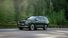 2022 Lincoln Navigator Black Label full-size luxury SUV in Manhattan Green driving on a highway past of a forest of evergreen trees