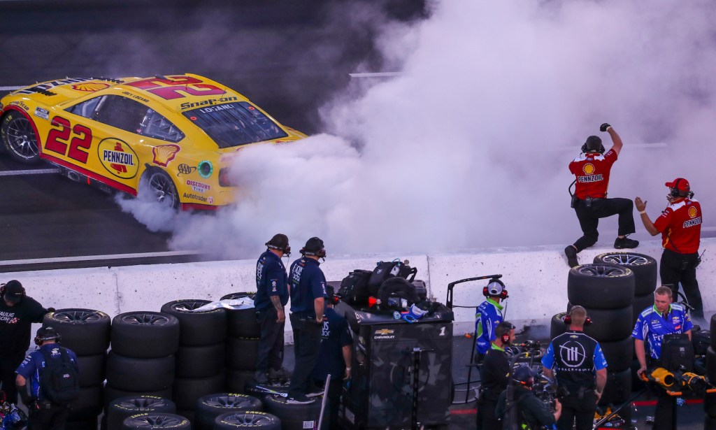 Driver Joe Logano popping his NASCAR Next Gen car's clutch and doing a burnout down pit road while his team cheers him on.