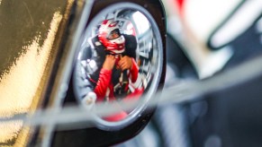 Closeup of the wing mirror on a NASCAR race car, reflecting the image of Bubba Wallace strapped into the driver's seat.