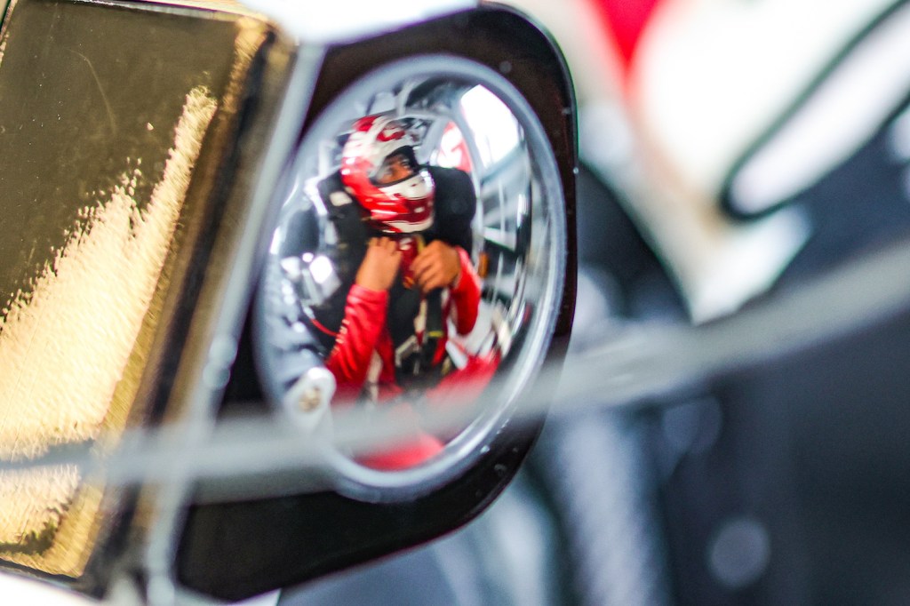 Closeup of the wing mirror on a NASCAR race car, reflecting the image of Bubba Wallace strapped into the driver's seat.